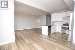 Open-concept kitchen and living area featuring wood-finish flooring, white cabinetry, dark countertops, and stainless steel appliances - 