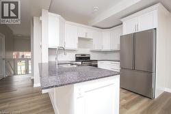 Modern kitchen featuring white shaker cabinetry, stainless steel appliances, a dark speckled countertop island with an undermount sink, and wood-finish flooring - 