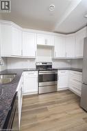 Kitchen featuring white shaker-style cabinetry, dark speckled countertops, stainless steel appliances, a white subway tile backsplash, and wood-finish flooring - 