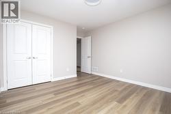 Spacious room featuring wood-finish flooring, light grey painted walls, white baseboards, and a contemporary ceiling light fixture - 