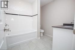 Bathroom featuring a white subway tile surround with a black accent border, a built-in bathtub with chrome fixtures, a modern vanity with a dark countertop, and light-toned floor tiling - 