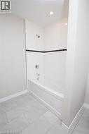 Bathtub and shower combination featuring white subway tile surround with a dark accent band, chrome fixtures, and recessed lighting - 
