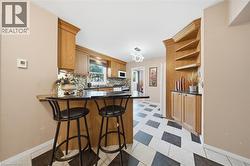 Kitchen featuring wood cabinetry, black countertops, checkerboard tile flooring, and built-in shelving with lower storage - 