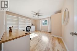 Spacious room featuring light wood-finish flooring, built-in shelving, a ceiling fan with integrated lighting, and a window with white trim - 