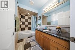 Bathroom featuring a soaking tub with checkerboard tile surround, a dark stone vanity countertop, wood-finish cabinetry, and a large wall-mounted mirror with integrated lighting - 