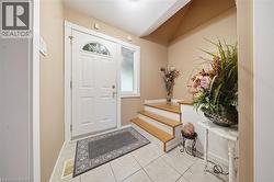Entryway featuring a white paneled door with an arched window, a frosted side window, light tile flooring, and a multi-level wood-finish staircase - 