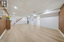Open-concept finished lower level featuring light wood-finish flooring, recessed lighting, white baseboards, and a wooden staircase with a banister - 