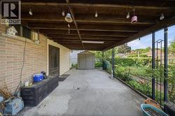 Covered concrete patio featuring an exposed wood beam ceiling, brick exterior wall, and a detached storage shed - 