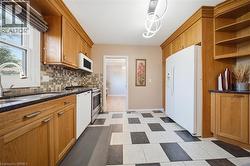 Kitchen featuring wood cabinetry, black and white checkerboard flooring, dark countertops, built-in microwave, and stainless steel sink - 