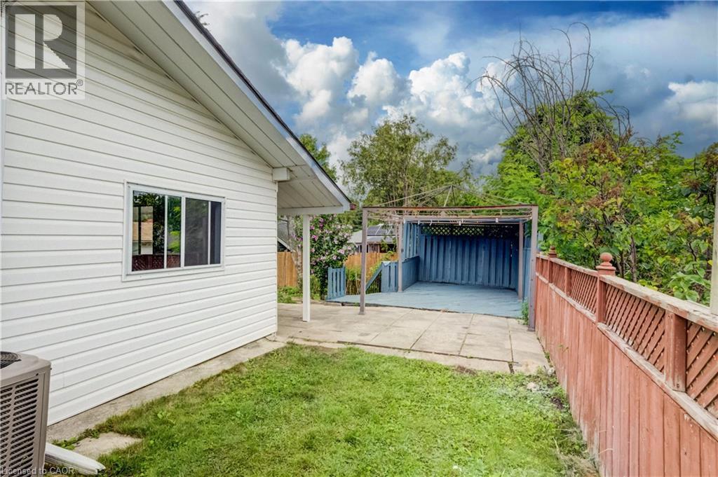 Rear exterior featuring white horizontal siding, a framed window, concrete patio, grassed area, and a red-stained wooden fence - 182 Avalon Place, Kitchener, ON - Outdoor With Exterior