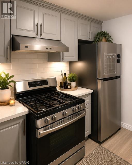 Kitchen featuring light grey cabinetry, a stainless steel range with overhead ventilation, a stainless steel refrigerator, white subway tile backsplash, and light wood-finish flooring - 143 Grenfell Place, London, ON - Indoor Photo Showing Kitchen