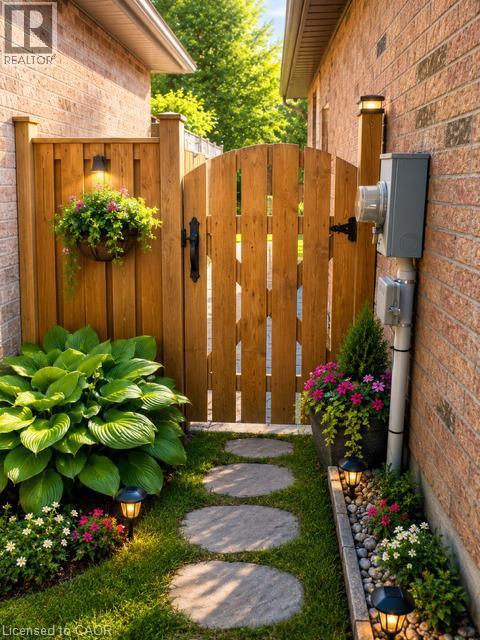 Private side yard access featuring a wood gate, stone stepping path, brick exterior, and integrated garden beds with lush plantings - 143 Grenfell Place, London, ON - Outdoor