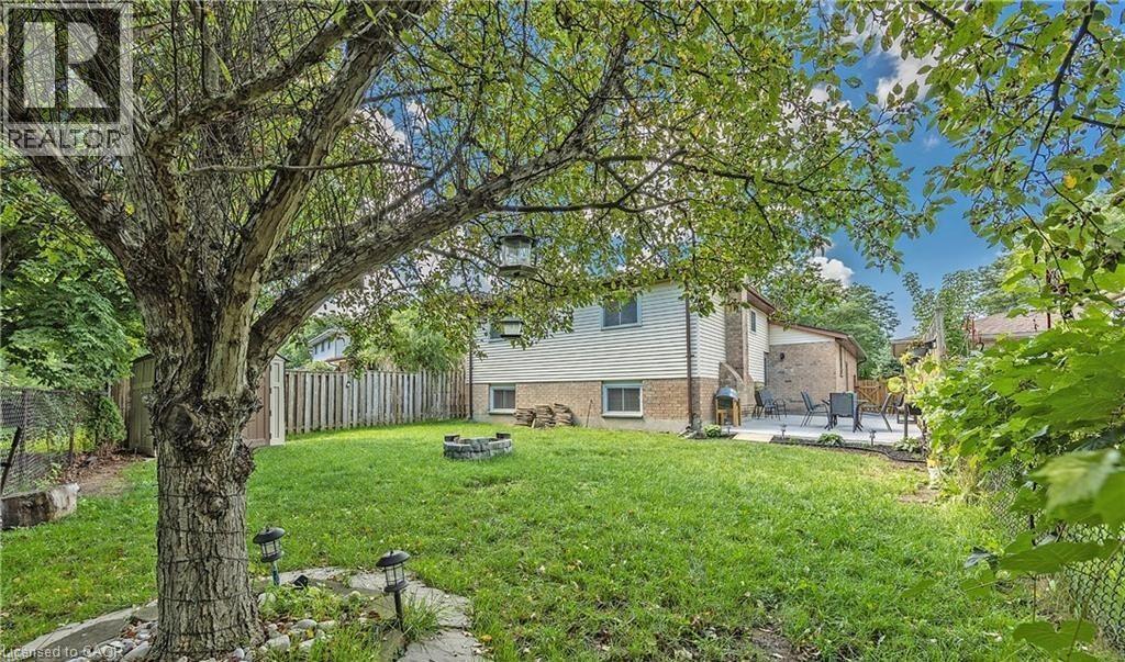 Expansive backyard featuring a mature tree, a stone-edged fire pit, a paved patio area, and perimeter fencing - 143 Grenfell Place, London, ON - Outdoor