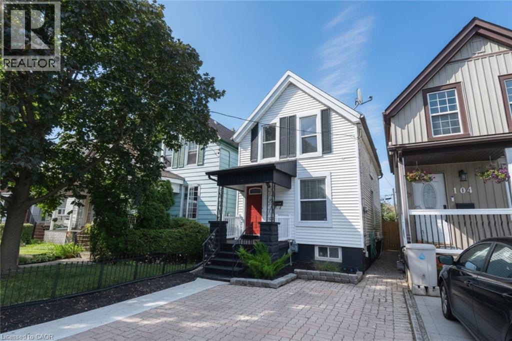 White-sided residential property featuring black window shutters and a covered porch with a red entry door - 106 Belview Avenue, Hamilton, ON - Outdoor With Facade