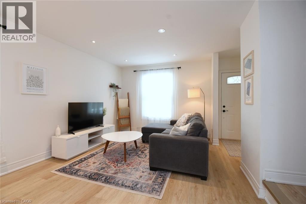 Living area featuring light wood-finish flooring, recessed lighting, a large window with sheer privacy coverings, and a white paneled entry door with frosted glass - 106 Belview Avenue, Hamilton, ON - Indoor Photo Showing Living Room