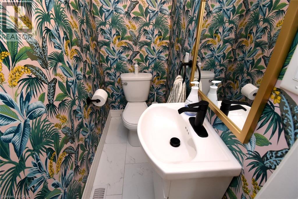 Powder room featuring botanical print wallpaper, white pedestal sink, matte black faucet, and a gold-framed mirror - 106 Belview Avenue, Hamilton, ON - Indoor Photo Showing Bathroom