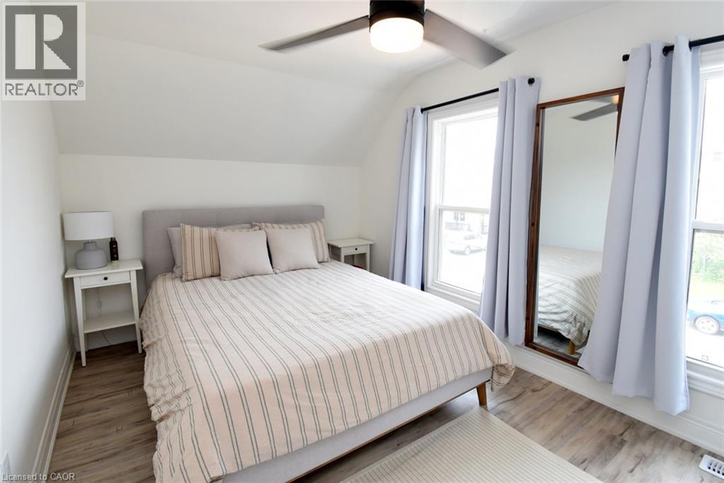 Bedroom featuring sloped ceilings, two window openings with light-colored drapes, wood-finish flooring, and a ceiling fan with integrated lighting - 106 Belview Avenue, Hamilton, ON - Indoor Photo Showing Bedroom