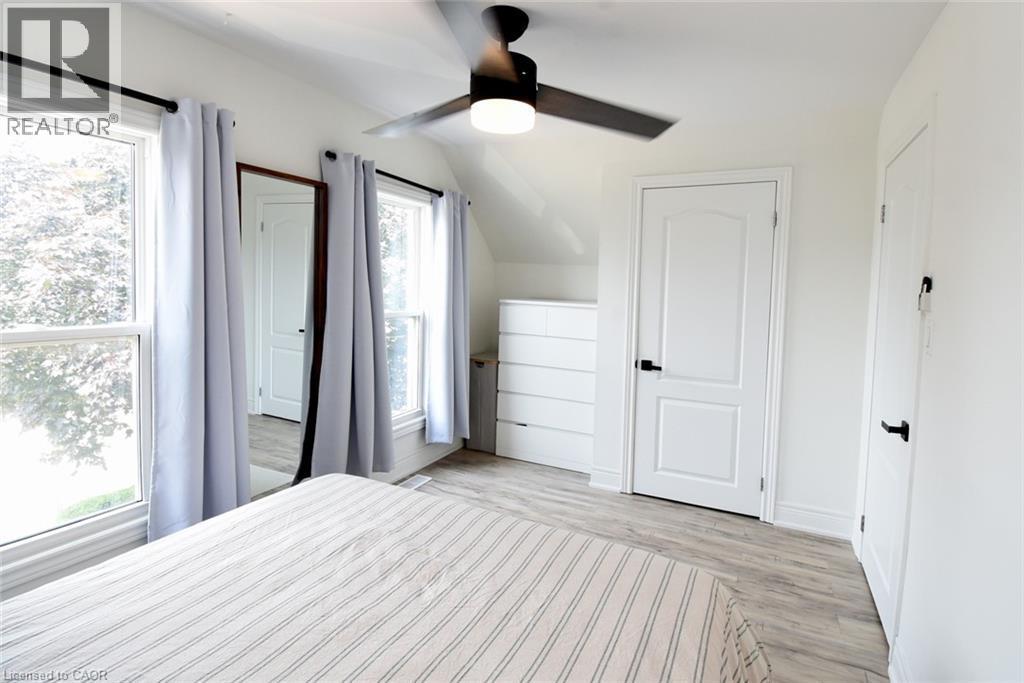 Bright interior space featuring two windows with white trim, a ceiling fan with integrated lighting, and light wood-finish flooring - 106 Belview Avenue, Hamilton, ON - Indoor Photo Showing Bedroom