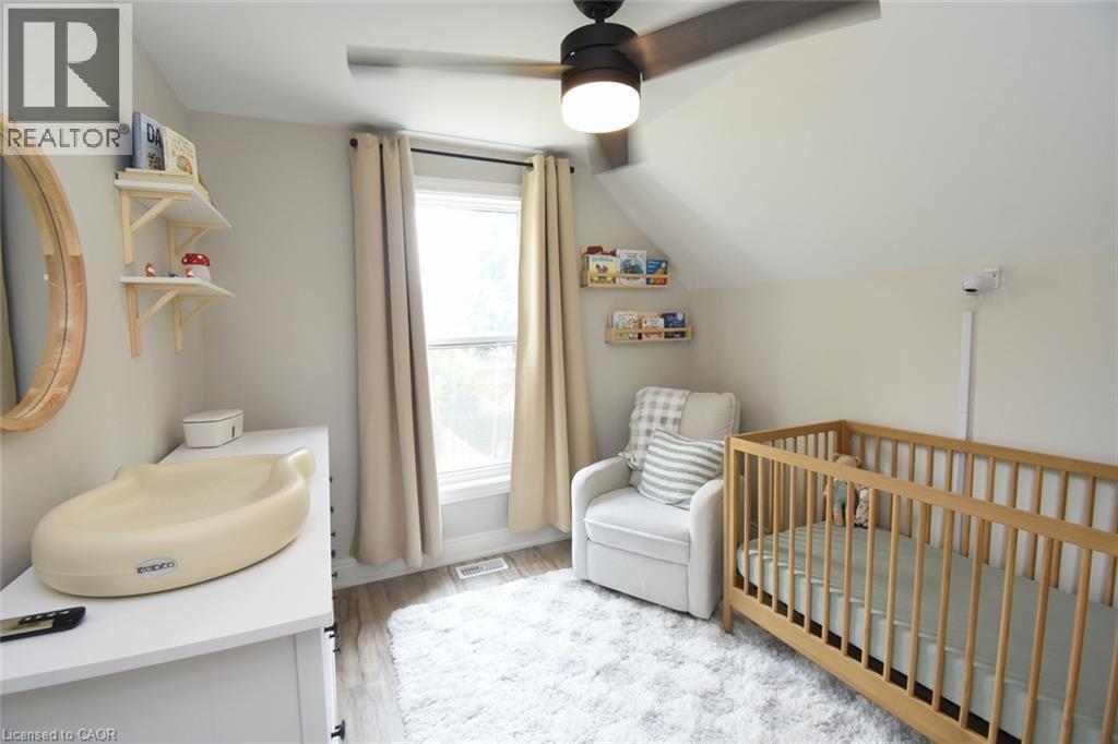 Bright room featuring sloped ceilings, a large window with drapes, wood-finish flooring, a contemporary ceiling fan with integrated lighting, and built-in shelving - 106 Belview Avenue, Hamilton, ON - Indoor Photo Showing Bedroom