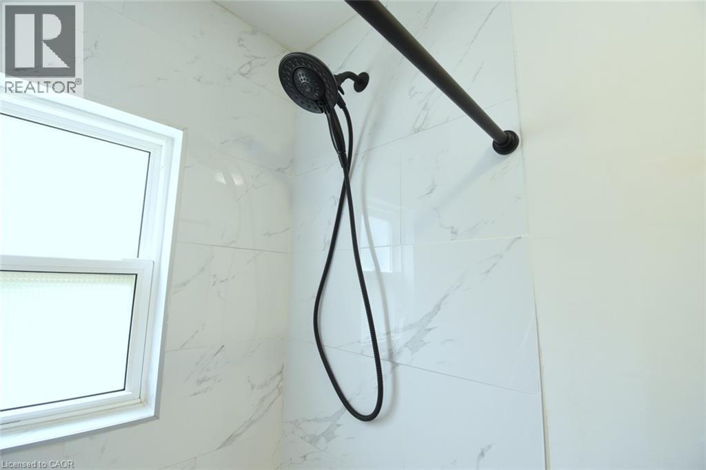 Shower enclosure featuring white marble-look wall tiling and a matte black shower head with an integrated handheld sprayer - 106 Belview Avenue, Hamilton, ON - Photo Showing Bathroom