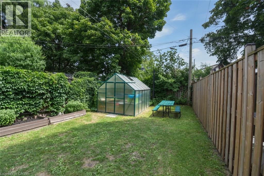 Fenced backyard featuring a greenhouse structure, a manicured lawn, raised garden beds, and mature perimeter trees - 106 Belview Avenue, Hamilton, ON - Outdoor