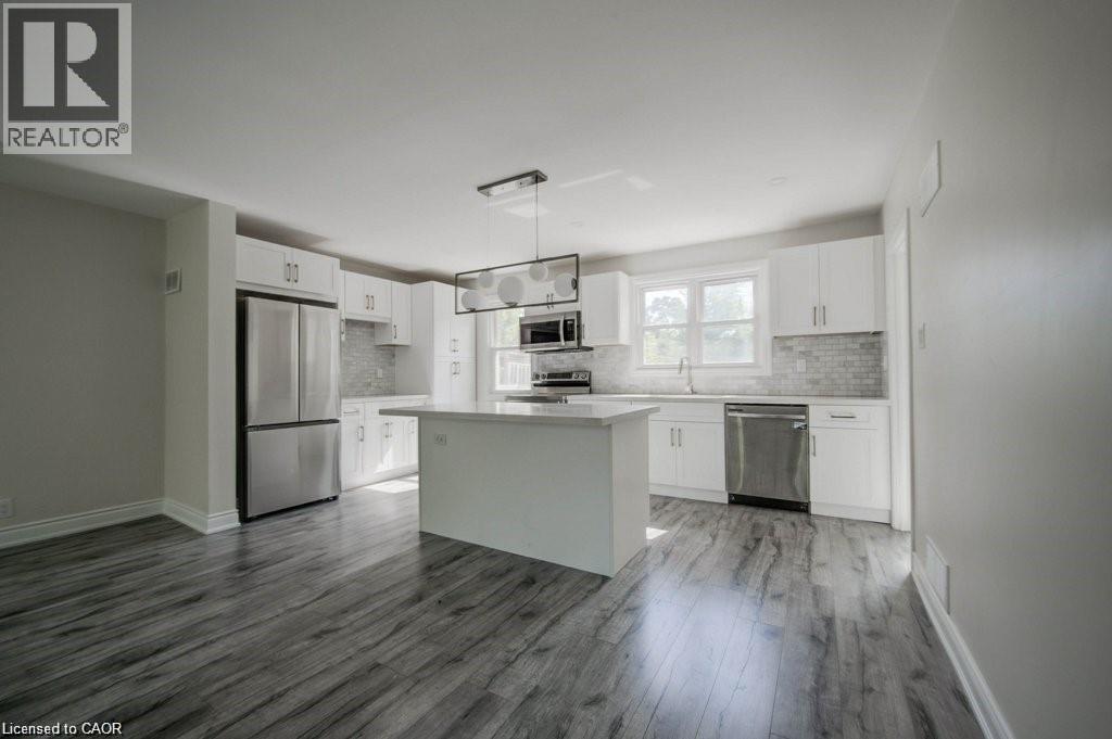 Open-concept kitchen featuring white cabinetry, stainless steel appliances, a central island, mosaic tile backsplash, and wood-finish flooring - 33 Sixth Avenue Unit# Upper, Kitchener, ON - Indoor Photo Showing Kitchen