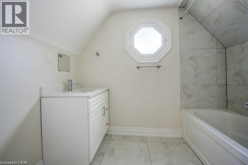 Contemporary bathroom featuring a white vanity with an integrated sink and chrome faucet, a unique octagonal window, a built-in bathtub with a tiled surround, and large format floor tiles - 33 Sixth Avenue Unit# Upper, Kitchener, ON - Indoor Photo Showing Bathroom