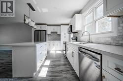 Kitchen featuring an oversized island with a white countertop, white shaker-style cabinetry with brushed nickel hardware, and wood-finish flooring -