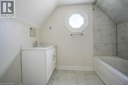 Contemporary bathroom featuring a white vanity with an integrated sink and chrome faucet, a unique octagonal window, a built-in bathtub with a tiled surround, and large format floor tiles -