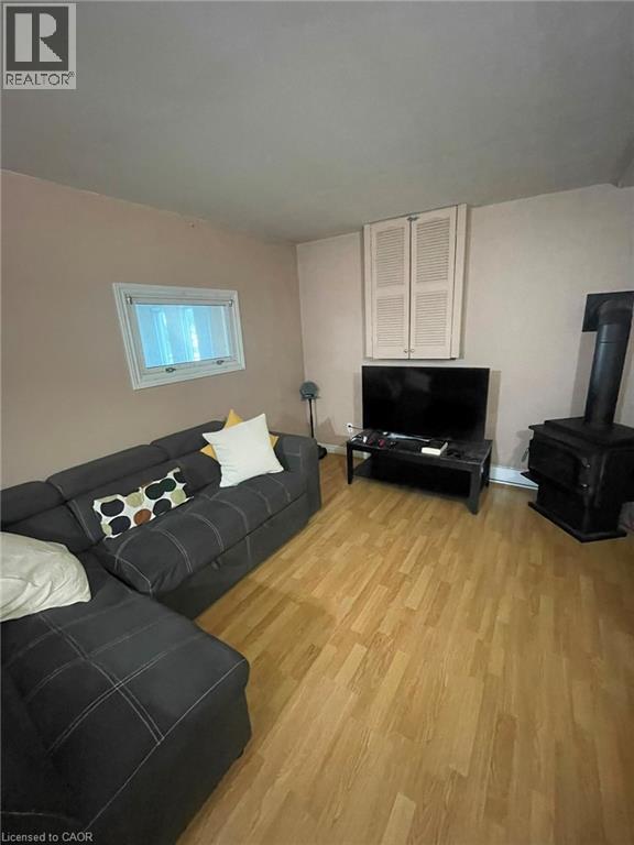 Living area featuring wood-finish flooring, a wall-mounted wood-burning stove, and a window with white trim - 267 Mackie Place Unit# 2, Kitchener, ON - Indoor Photo Showing Living Room