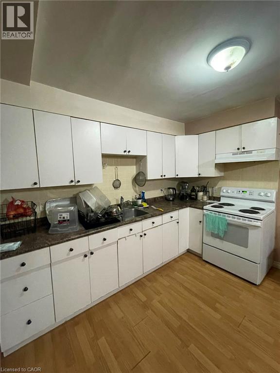 Kitchen featuring abundant white cabinetry, a corner sink, a freestanding white range, dark speckled countertops, and wood-finish flooring - 267 Mackie Place Unit# 2, Kitchener, ON - Indoor Photo Showing Kitchen With Double Sink