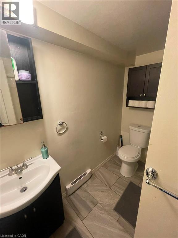Compact bathroom featuring a white ceramic toilet, a vanity with a white basin and dark cabinetry, and neutral-toned wall paint - 267 Mackie Place Unit# 2, Kitchener, ON - Indoor Photo Showing Bathroom
