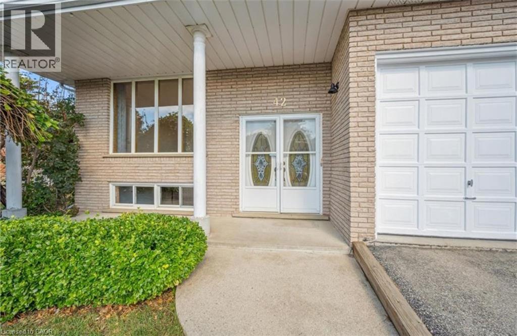 Brick exterior featuring a covered entry porch supported by white columns, double front doors with decorative glass inserts, a single-car garage with a panelled door, and a concrete pathway with manic - 42 Azores Crescent, Cambridge, ON - Outdoor With Exterior
