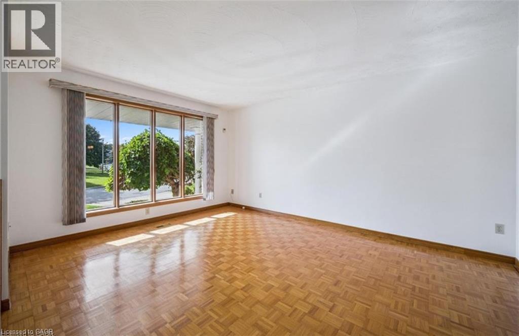 Bright interior space featuring a large picture window with wood-finish trim, parquet wood flooring, white walls, and a textured white ceiling - 42 Azores Crescent, Cambridge, ON - Indoor Photo Showing Other Room