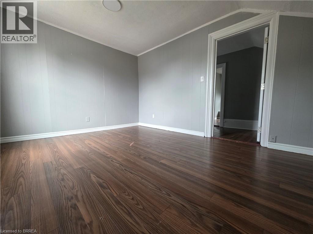 Spacious interior room featuring wood-finish flooring, light gray wall paneling, and white trim - 109 Sydenham Street, Brantford, ON - Indoor Photo Showing Other Room