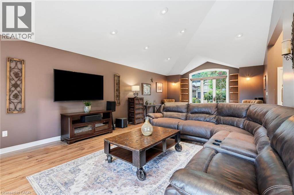 Vaulted ceiling living area featuring wood-finish flooring, a prominent arched window, recessed lighting, and built-in shelving - 5 Manor Crescent, Grimsby, ON - Indoor Photo Showing Living Room