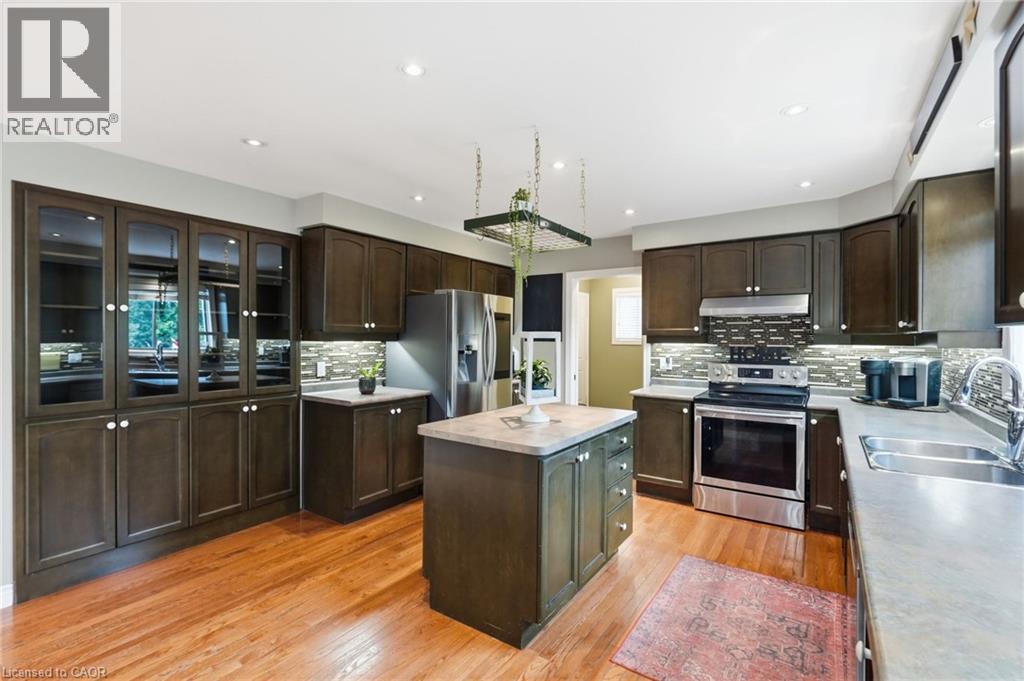 Gourmet kitchen featuring dark wood cabinetry, a central island with a light-toned countertop, stainless steel appliances, and wood-finish flooring - 5 Manor Crescent, Grimsby, ON - Indoor Photo Showing Kitchen With Double Sink With Upgraded Kitchen