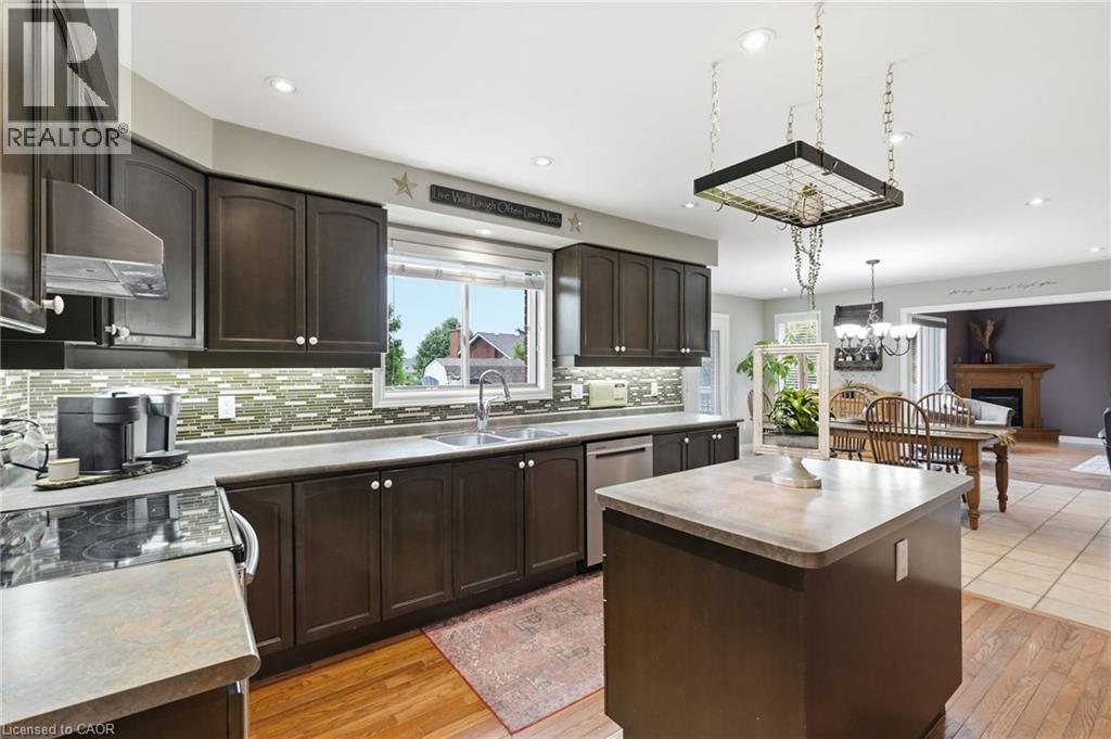 Kitchen featuring dark wood-finish cabinetry, a mosaic tile backsplash, stainless steel appliances, and a central island with a solid surface countertop - 5 Manor Crescent, Grimsby, ON - Indoor Photo Showing Kitchen With Double Sink