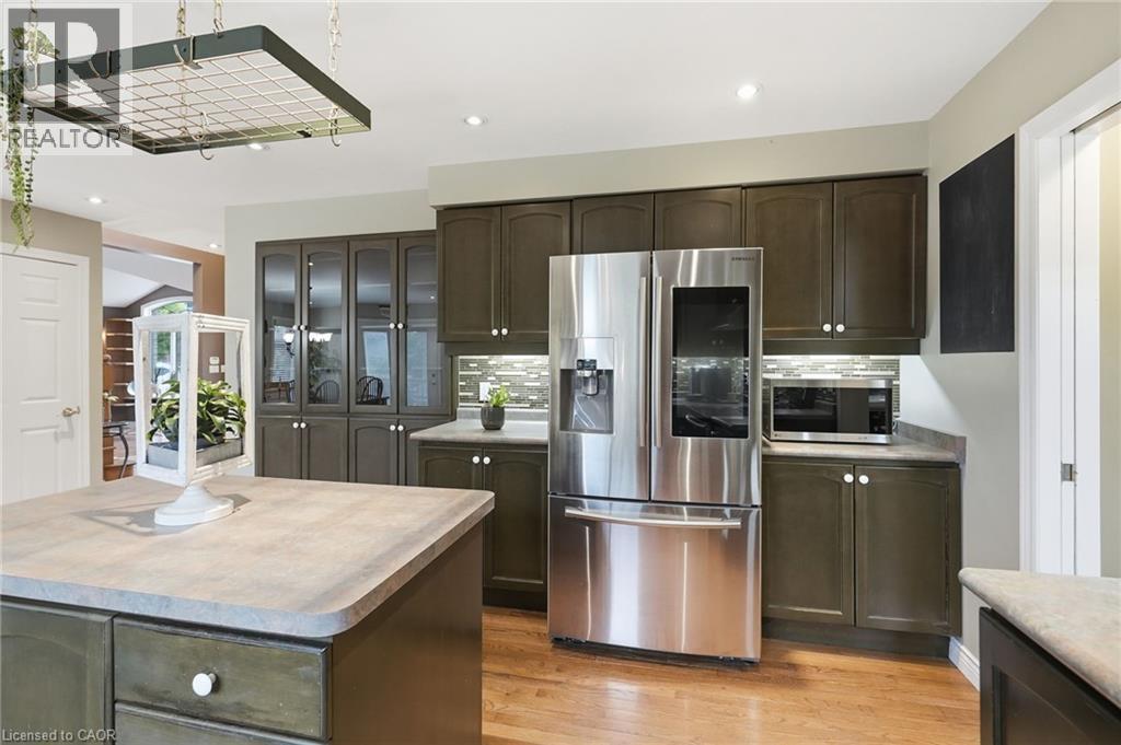 Kitchen featuring dark cabinetry, stainless steel refrigerator, undermount lighting, tile backsplash, and wood-finish flooring - 5 Manor Crescent, Grimsby, ON - Indoor Photo Showing Kitchen