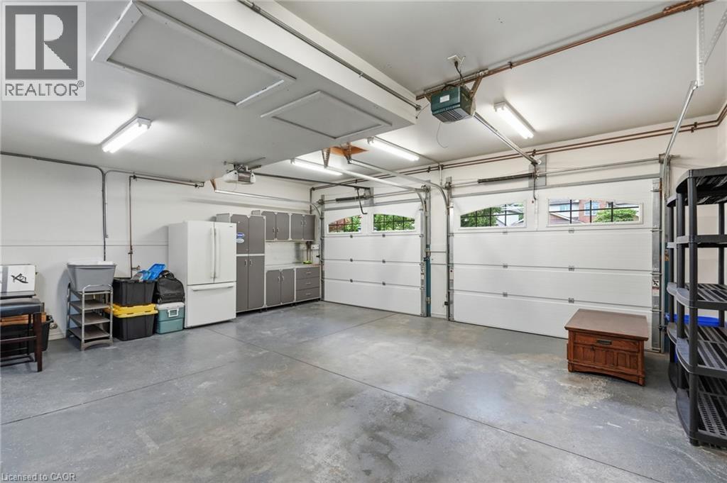 Spacious two-car garage featuring a concrete floor, two white garage doors with upper windows, and fluorescent overhead lighting - 5 Manor Crescent, Grimsby, ON - Indoor Photo Showing Garage