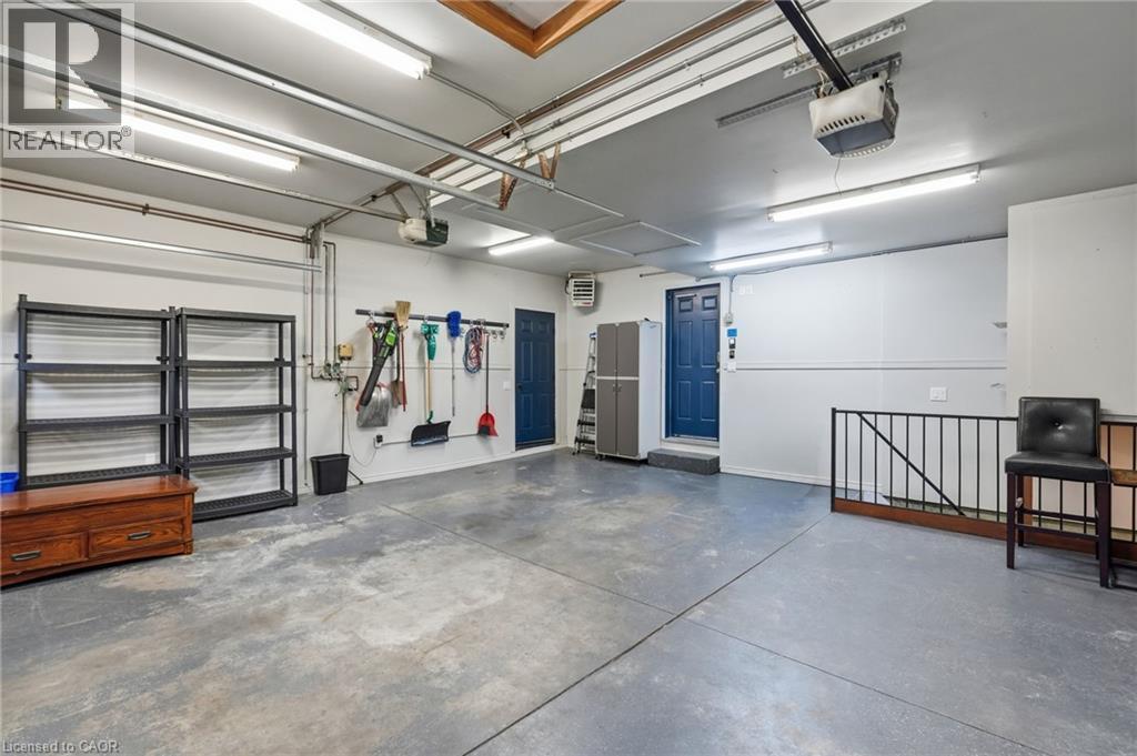 Spacious garage featuring a concrete floor, multiple fluorescent light fixtures, and a painted blue entry door - 5 Manor Crescent, Grimsby, ON - Indoor Photo Showing Garage