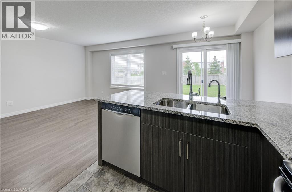 Kitchen island with granite countertop, double stainless steel sink, and contemporary dark wood-finish cabinetry - 823 Paris Boulevard, Waterloo, ON - Indoor Photo Showing Kitchen With Double Sink With Upgraded Kitchen