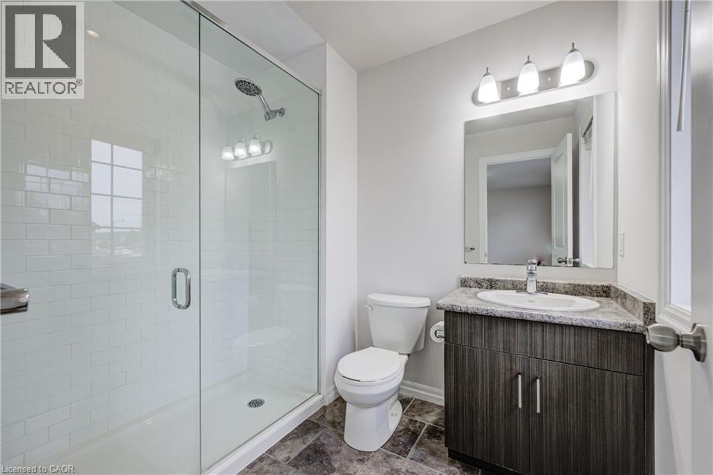 Contemporary bathroom featuring a glass-enclosed shower with white subway tile, a dark wood-finish vanity with a built-in sink and stone countertop, and a vanity mirror with a three-light fixture - 823 Paris Boulevard, Waterloo, ON - Indoor Photo Showing Bathroom