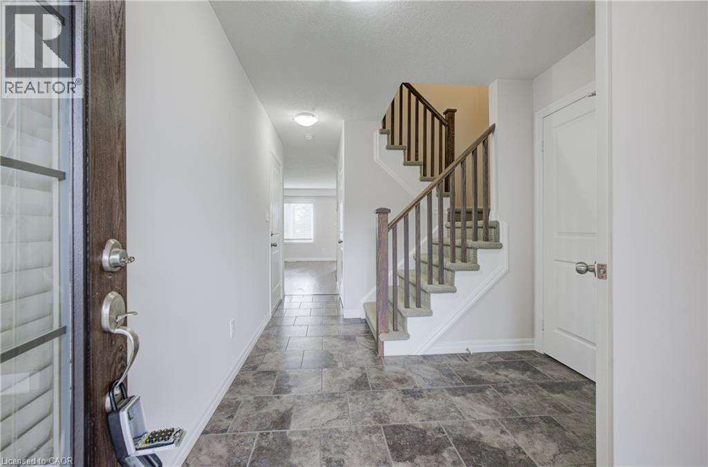 Foyer featuring slate-look tile flooring, a wood-finish entry door with clear glass panels, a staircase with wood-finish railings, and a corridor leading to additional interior spaces - 823 Paris Boulevard, Waterloo, ON - Indoor Photo Showing Other Room