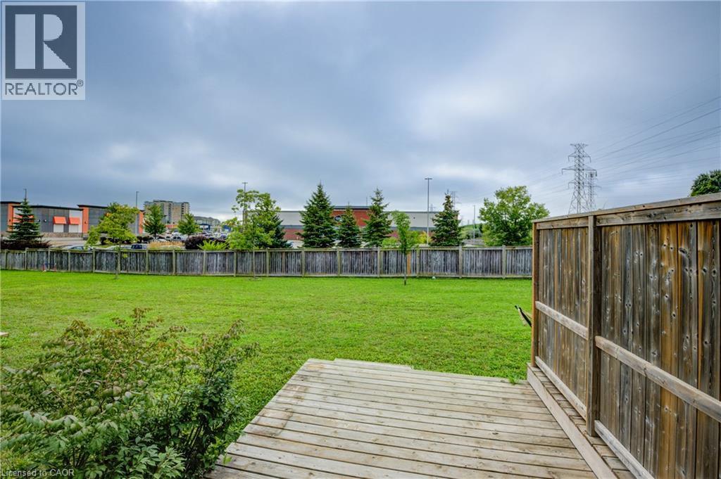 Backyard featuring a wooden deck, a spacious lawn, a perimeter wooden fence, and mature evergreen trees lining the property line - 823 Paris Boulevard, Waterloo, ON - Outdoor With Deck Patio Veranda