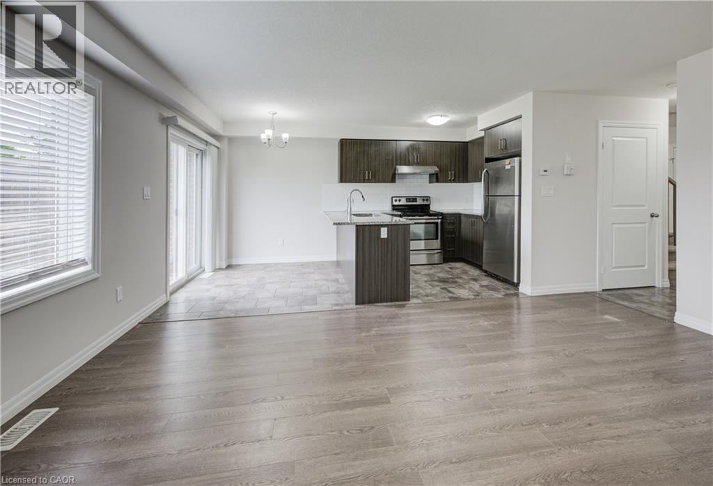 Open-concept living space featuring wood-finish flooring, a kitchen island with a stainless steel sink, dark wood-finish cabinetry, and stainless steel appliances - 823 Paris Boulevard, Waterloo, ON - Indoor Photo Showing Kitchen