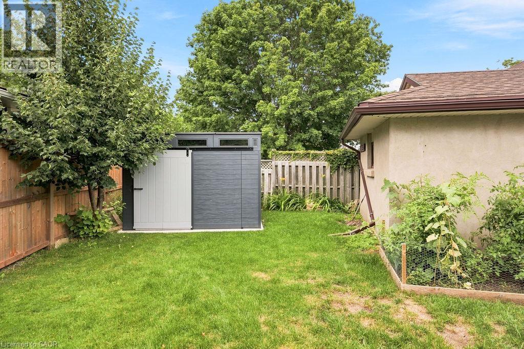 Expansive backyard featuring a modern two-tone storage shed with transom windows, a wood fence perimeter, and mature trees - 67 Weber Street S, Waterloo, ON - Outdoor