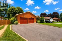 Brick exterior featuring a two-car garage with red doors, a paved driveway, and established front landscaping - 