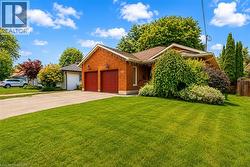 Brick exterior featuring a two-car garage with red doors, a paved driveway, and mature landscaping - 