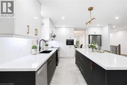 Modern kitchen featuring a large central island with a white countertop, two-tone cabinetry with gold-finish hardware, stainless steel appliances, and recessed lighting - 